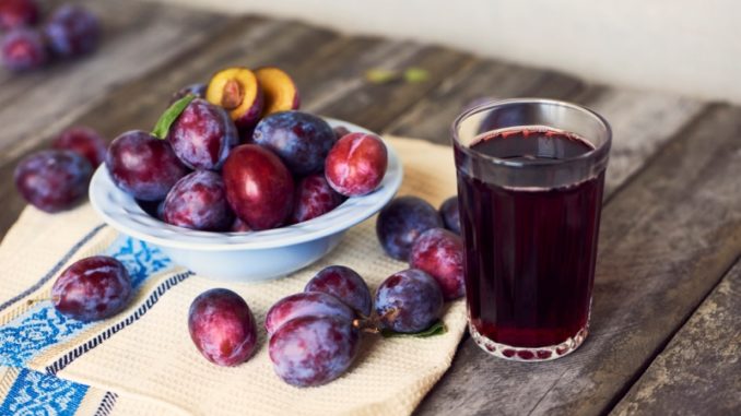 Glass of plum juce with fresh fruits in plate on wooden background